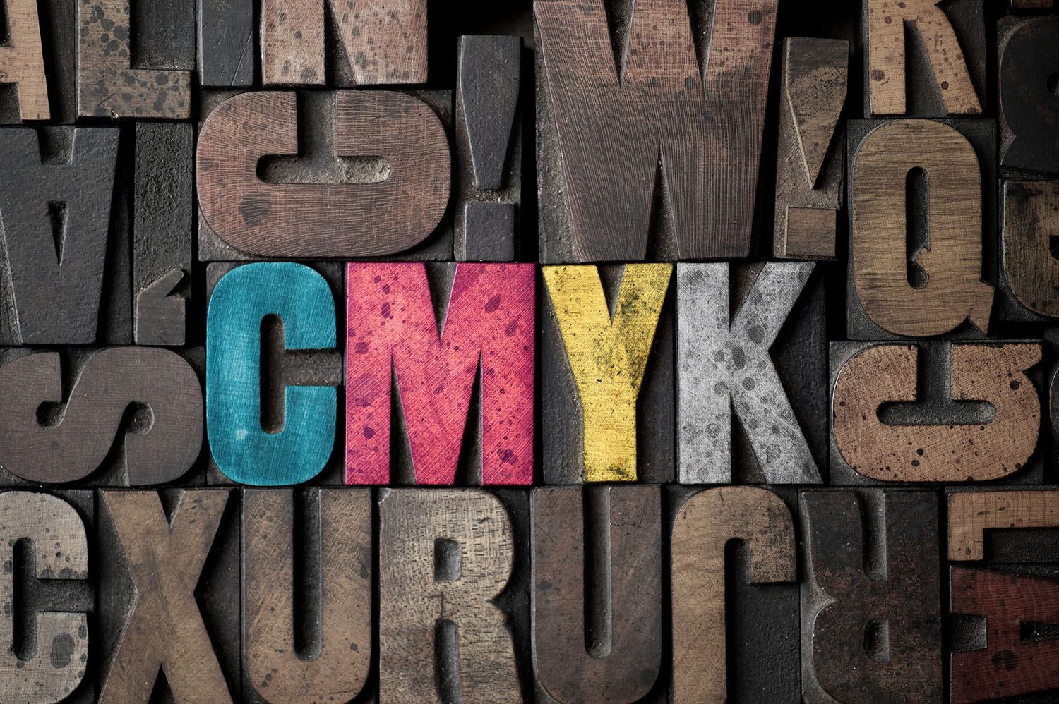 The letters 'CMYK' spelled out in very old letterpress blocks.